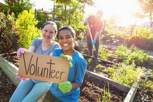 Portrait of Hispanic young woman and Caucasian young woman students hold volunteer sign together in success support achievement determination as youth organization volunteer charity in local community garden in residential district in summer